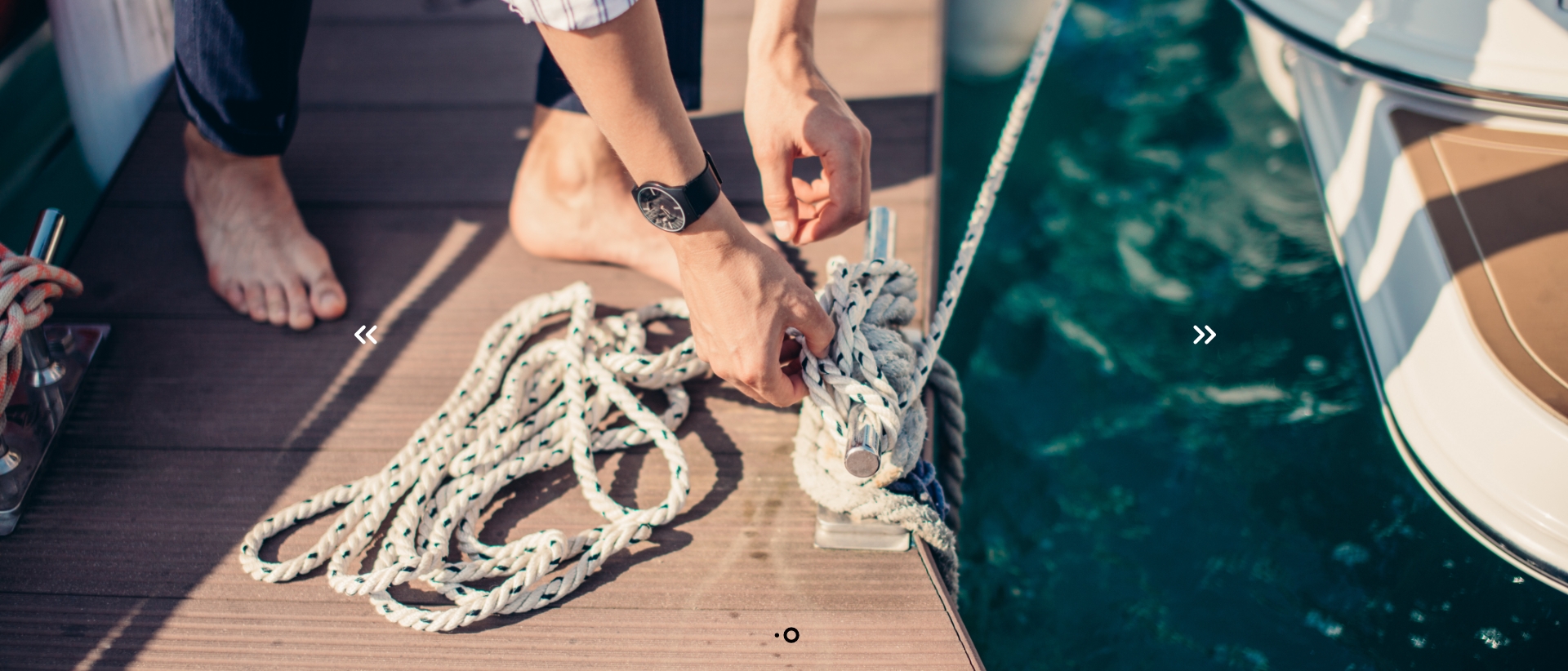 Man standing barefoot on a dock tying up his boat with rope to a dock cleat